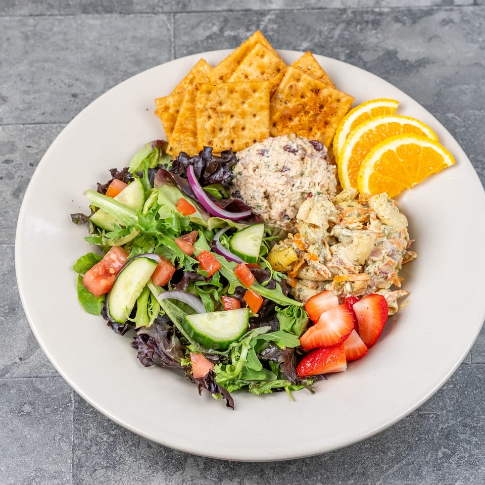 Plate of mixed green salad, creamy pasta and chicken salads, crackers, orange slices, and strawberries.